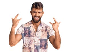 Yaz kıyafetleri giymiş, çılgın bir ifadeyle bağıran İspanyol genç adam elleri havada rock sembolü yapıyor. Müzik yıldızı. ağır kavram. 