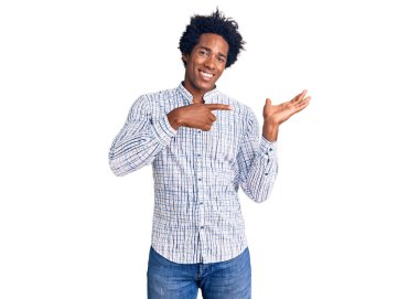 Yakışıklı Afro saçlı, sıradan kıyafetler giyen, kameraya hayret eden ve gülümseyen, eli ve parmağıyla işaret eden Afro-Amerikan bir adam.. 