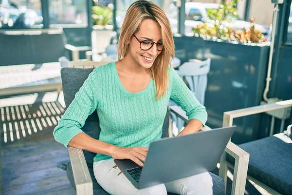 年轻的金发女人笑着高兴地坐在咖啡店的阳台上 用笔记本电脑工作 — 图库照片