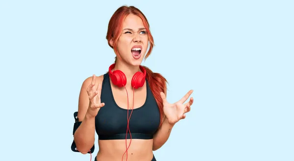 若い赤毛の女性はジムの服を着て 積極的な表現と腕を上げて 狂気と狂気の叫びと叫びをヘッドフォンを使用しています フラストレーションコンセプト — ストック写真