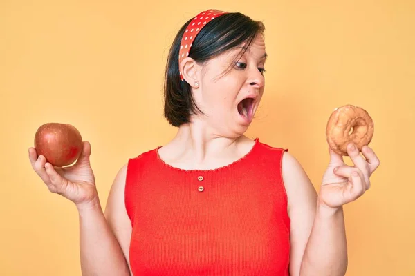 Μελαχρινή Γυναίκα Σύνδρομο Κρατώντας Κόκκινο Μήλο Και Ντόνατ Κάθεται Θυμωμένος — Φωτογραφία Αρχείου