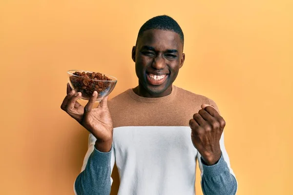 Joven Hombre Afroamericano Sosteniendo Tazón Con Pasas Gritando Orgulloso Celebrando — Foto de Stock