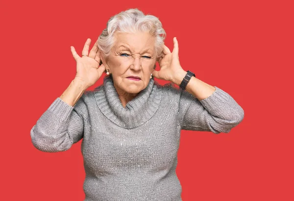 シニア白髪の女性が耳のジェスチャーで両方の手を聞くしようとしてカジュアルな冬のセーターを着て ゴシップへの好奇心 聴覚障害や聴覚障害 — ストック写真