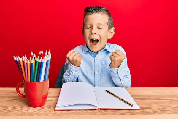 Criança Caucasiana Adorável Escrevendo Livro Sentado Mesa Comemorando Surpreso Surpreso — Fotografia de Stock