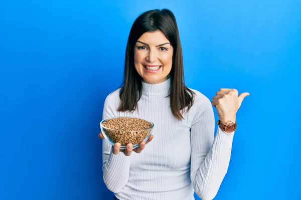 Young Hispanic Woman Holding Lentils Bowl Pointing Thumb Side Smiling — 图库照片