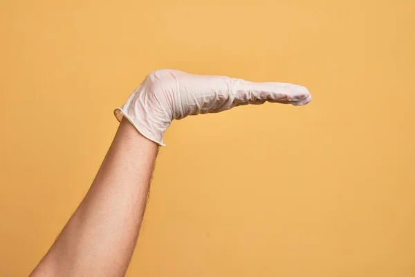 Mão Homem Jovem Caucasiano Com Luva Médica Sobre Fundo Amarelo — Fotografia de Stock