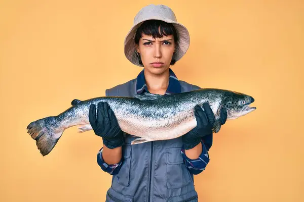 Hermosa Mujer Pescadora Morena Mostrando Salmón Crudo Escéptico Nervioso Frunciendo —  Fotos de Stock