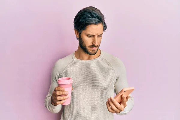 Joven Hombre Hispano Usando Smartphone Bebiendo Una Taza Café Escéptico —  Fotos de Stock