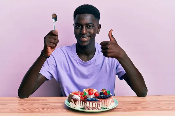Νεαρός Αφροαμερικάνος Κάθεται Στο Τραπέζι Τρώγοντας Κέικ Χαμογελώντας Χαρούμενος Και — Φωτογραφία Αρχείου