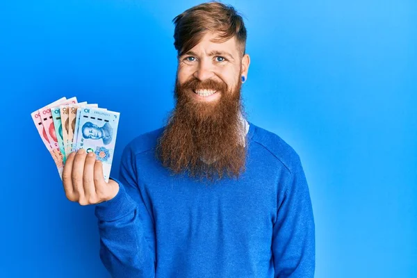 Genç İrlandalı kızıl saçlı adam Yuan Çin banknotlarını tutuyor. Pozitif ve mutlu görünüyor. Kendine güvenen bir gülümsemeyle dişlerini gösteriyor. 