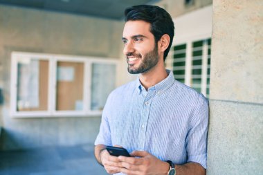 Genç İspanyol adam şehirde akıllı telefon kullanarak mutlu gülümsüyor..