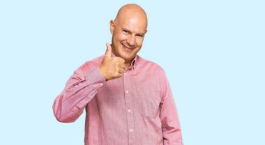 Orta yaşlı, kel, sıradan kıyafetler giyen mutlu baş parmaklar hareketi yapan bir adam. Kameraya bakıp başarıyı gösteren ifade. 