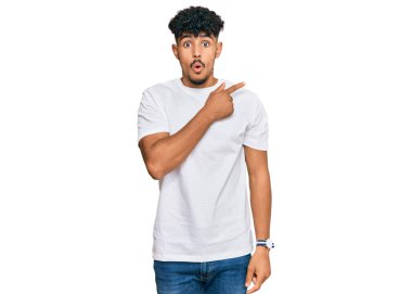 Gündelik beyaz t-shirt giyen genç Arap adam parmaklarını yana doğru göstererek şaşırdı, ağzı açık hayret içinde kaldı.. 