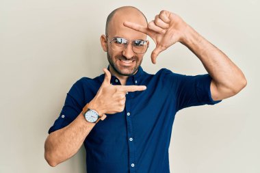 Gündelik kıyafetler ve gözlük takan genç İspanyol adam gülümsüyor ve mutlu yüzlü eller ve parmaklarla çerçeve yapıyor. yaratıcılık ve fotoğrafçılık kavramı. 