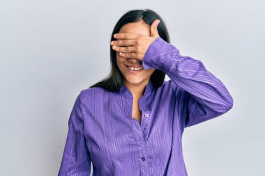 Genç esmer kadın, günlük kıyafetler giyiyor, gülümsüyor ve elleri yüzünde, şaşırtmak için gözleri örtüyor. kör kavram. 