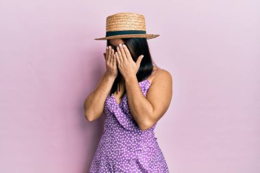 Genç esmer kadın, yaz elbisesi ve ağlarken suratını ellerle kapatan üzgün bir şapkayla. depresyon kavramı. 