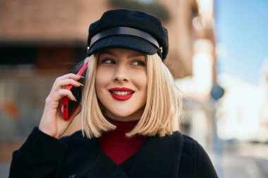 Genç sarışın kadın gülümsüyor. Şehirdeki akıllı telefondan konuşuyor..