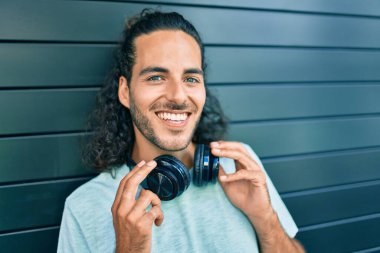 Genç İspanyol gülümseyen adam şehirde kulaklık takarak müzik dinlemekten mutlu oluyor..