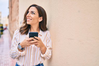 Genç İspanyol kadın şehirde akıllı telefon kullanarak mutlu bir şekilde gülümsüyor..