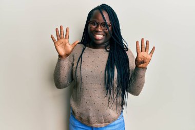 Saçları örgülü, günlük kıyafetler giyen ve gözlüklü genç siyahi bir kadın dokuz numarayı gösterip işaret ederken kendinden emin ve mutlu bir şekilde gülümsüyor.. 