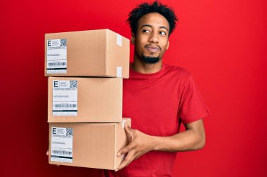 Sakallı, teslimat paketleri taşıyan, gülümseyen ve kafasını çeviren genç Afro-Amerikan bir adam.. 