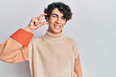 İspanyol genç adam, sıradan bir süveter giyiyor gülümsüyor ve el hareketleriyle hareket ediyor parmaklarıyla işaret yapıyor ve kameraya bakıyor. ölçüm kavramı. 