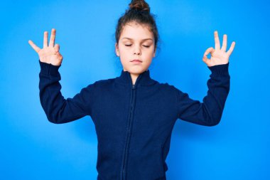 Hoş İspanyol çocuk günlük kıyafetler giyip rahatlıyor ve gözleri kapalı gülümsüyor parmaklarıyla meditasyon hareketi yapıyor. yoga konsepti. 