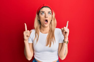 Gündelik beyaz tişört giyen genç beyaz kadın şaşkın şaşkın yukarı bakıyor ve parmaklarıyla işaret ediyor ve kollarını kaldırıyordu.. 