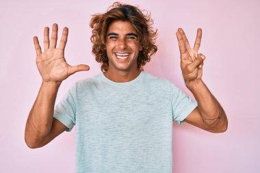 Gündelik kıyafetler giyen genç İspanyol adam sekiz numarayı gösterip işaret ederken kendinden emin ve mutlu bir şekilde gülümsüyor.. 