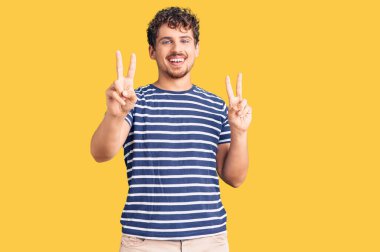 Kıvırcık saçlı, sıradan giyinmiş, gülümseyen, parmaklarını zafer işareti yaparken gösteren genç, yakışıklı bir adam. İki numara.. 