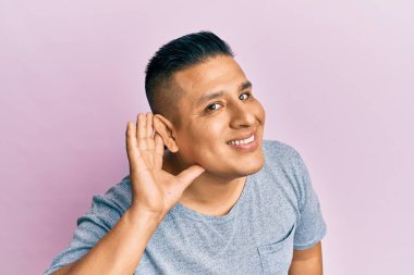 Gündelik kıyafetler giyen genç latin adam kulağından kulaklarına gülümseyerek dedikodu ya da dedikoduları dinliyor. Sağırlık kavramı. 