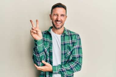 Sakallı, sıradan kıyafetler giyen, gülümseyen, kameraya göz kırpan ve zafer işareti yapan yakışıklı bir adam. İki numara.. 