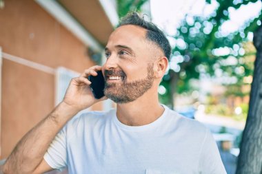 Orta yaşlı yakışıklı adam şehirde akıllı telefon kullanarak mutlu gülümsüyor..