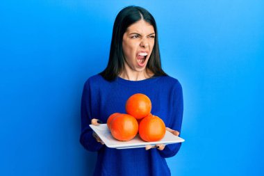 Genç İspanyol kadın elinde taze portakallarla kızgın ve kızgın çığlıklar atıyor öfkeyle bağırıyor. öfke ve agresif konsept. 