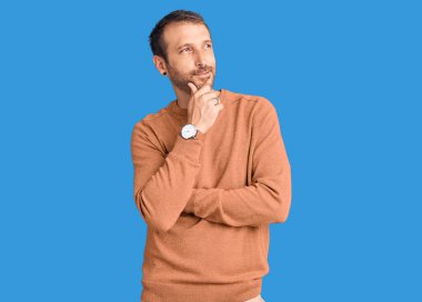 Elleri çenesinde gündelik giysiler giymiş soru soran, düşünceli bir genç adam. Düşünceli bir yüzle gülümsüyor. şüphe kavramı. 