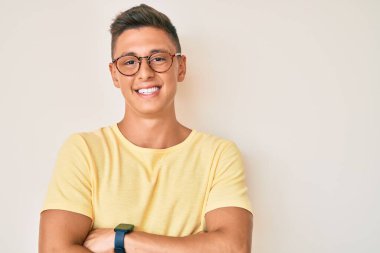 Sıradan kıyafetler ve gözlük takan, kolları çapraz gülümseyen ve kameraya bakan genç İspanyol çocuk. pozitif kişi. 