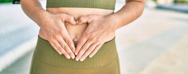 Spor giyinen bir kadın. Şehirde elleri karnının üstünde..