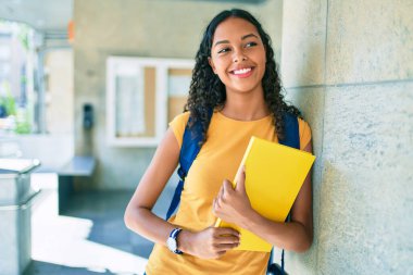 Genç Afrikalı Amerikalı öğrenci mutlu gülümsüyor ve üniversitede kitap tutuyor..