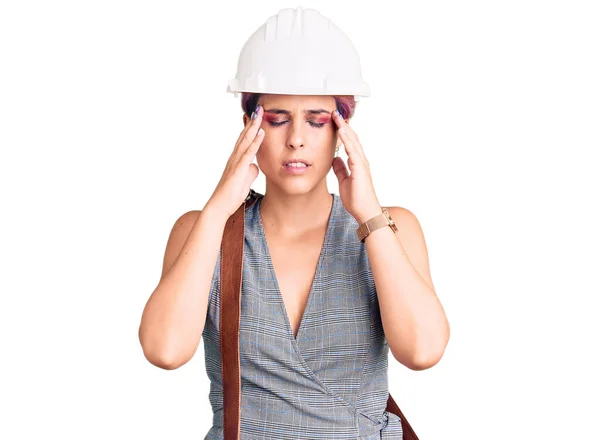 年轻美丽的女人戴着建筑师的硬礼帽 头戴皮包 由于疼痛和偏头痛 压力重重 手放在头上 — 图库照片