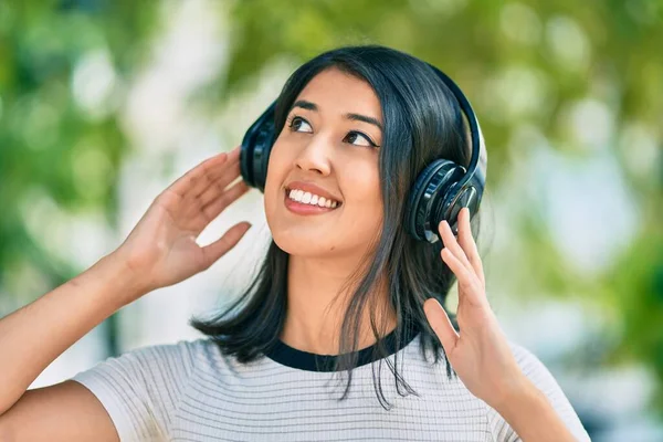 Genç İspanyol kadın gülümseyerek şehirde kulaklık takarak müzik dinliyor..