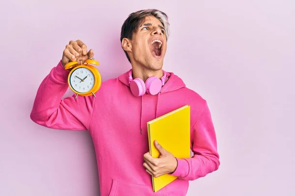 Young Hispanic Man Holding Book Alarm Clock Angry Mad Screaming — Zdjęcie stockowe