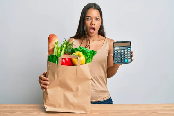 Beautiful Hispanic Woman Holding Groceries Calculator Afraid Shocked Surprise Amazed —  Fotos de Stock