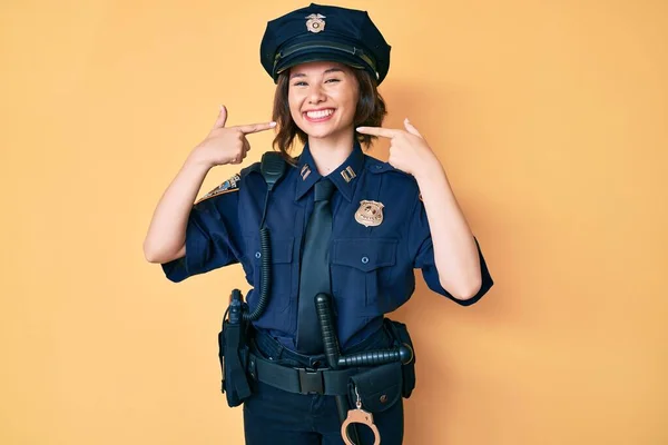 Young beautiful woman wearing police uniform smiling cheerful showing and pointing with fingers teeth and mouth. dental health concept.