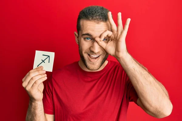 Young Caucasian Man Holding Paper Sagittarius Zodiac Sign Smiling Happy — Stock Photo, Image