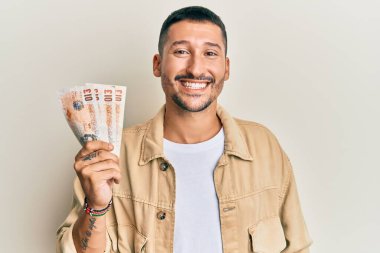 Dövmeleri olan yakışıklı bir adam, elinde 10 pound banknot tutuyor. Pozitif ve mutlu görünüyor. Kendine güvenen bir gülümsemeyle dişlerini gösteriyor. 