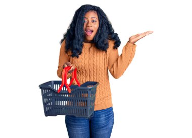 Güzel Afro-Amerikalı kadın elinde süpermarket alışveriş sepeti tutarak zaferi mutlu bir gülümsemeyle ve kazanan yüz ifadesiyle kutluyor. 