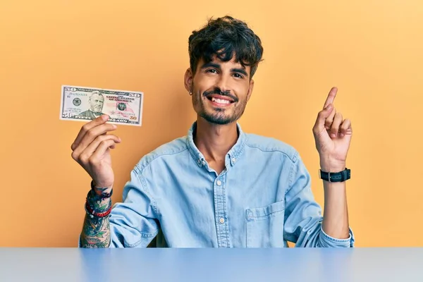 Jovem Hispânico Segurando Nota Dólares Sentado Mesa Sorrindo Feliz Apontando — Fotografia de Stock
