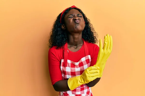 Beautiful African Young Woman Wearing Cleaner Apron Gloves Puffing Cheeks — Stockfoto
