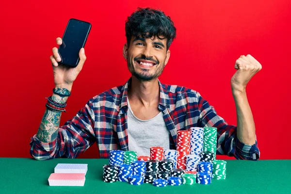 Mladý Hispánec Sedí Stole Pokerových Žetonů Karet Drží Smartphone Křičí — Stock fotografie