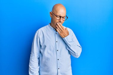 Orta yaşlı kel bir adam günlük giysiler ve gözlük takmış. Ağzı eliyle kapatmaktan sıkılmış. Huzursuz ve uykulu.. 